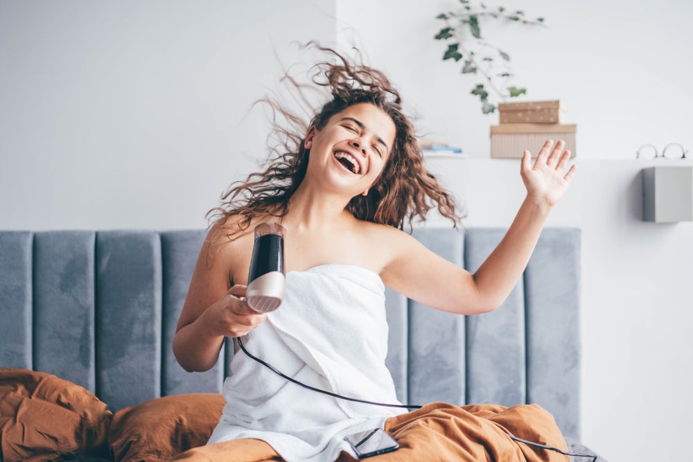 wet haired girl blow drying hair on bed singing